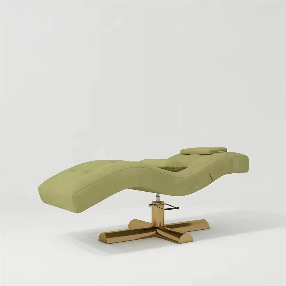 Sage green spa facial bed with a contoured, padded seat, adjustable headrest, and gold-finish cross base.