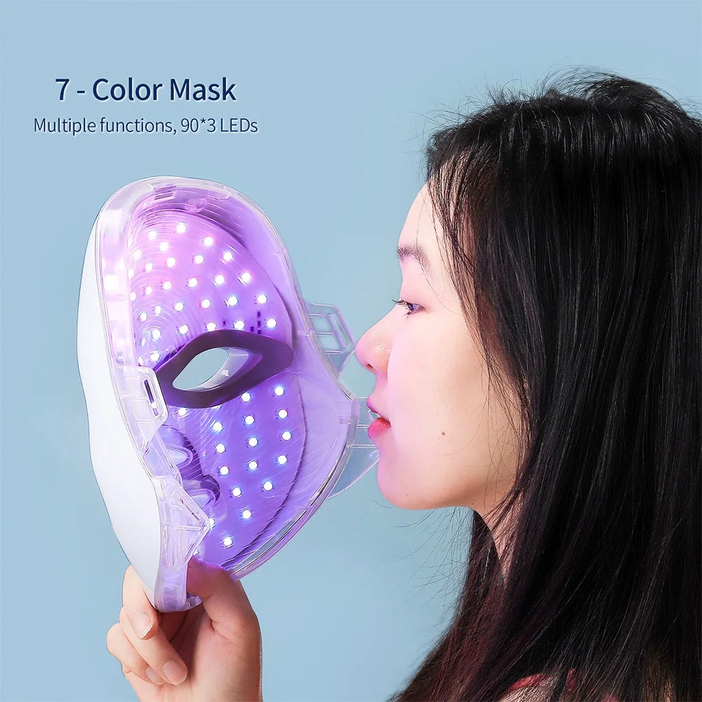 A woman holds a transparent, white-framed LED light therapy face mask emitting a bright purple glow.