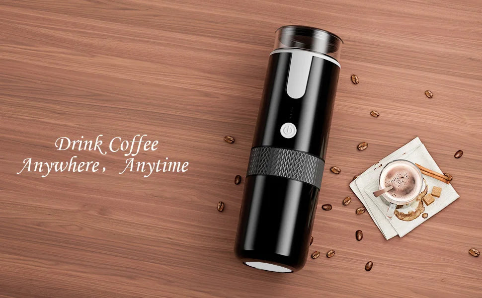 Portable black electric coffee maker with textured grip and power button on a wooden table with coffee beans and cup.