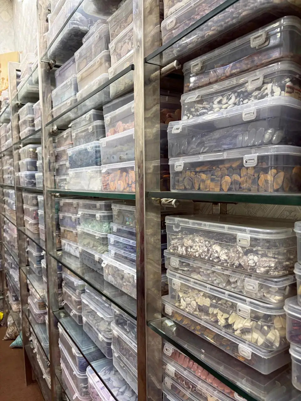 Clear plastic gemstone storage boxes on shelving, assorted mixed stones
