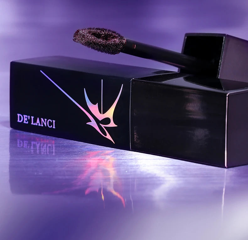 DE'LANCI gothic shimmer lip mud with dark blue glitter texture and applicator on a purple background.