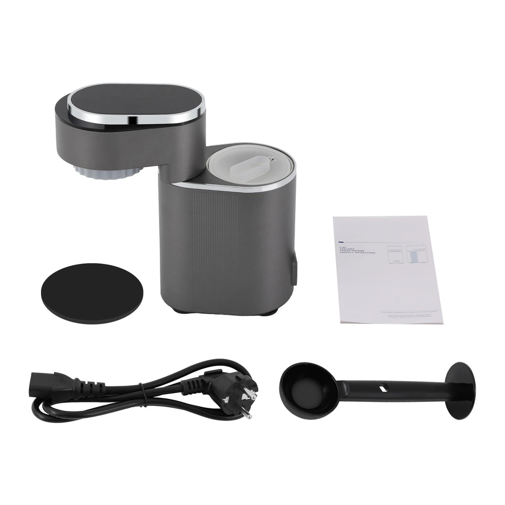 Portable dark gray electric coffee maker set with power cord, measuring scoop, and user manual on white background.