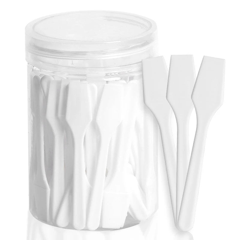 A clear plastic jar filled with small, white plastic cosmetic spatula scoops.