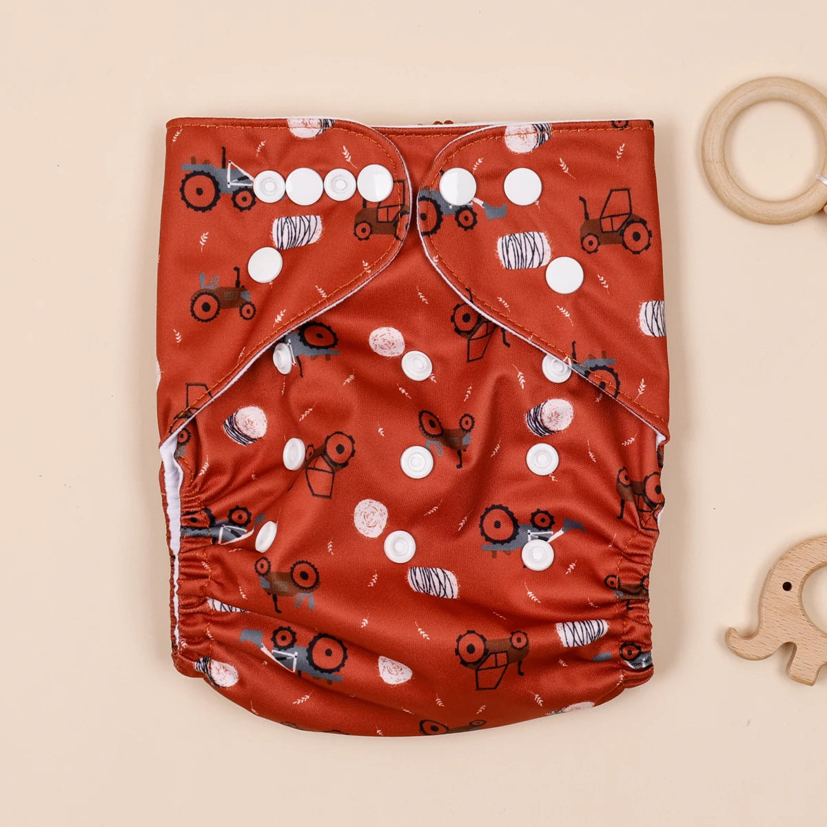 Reusable baby diaper with rust tractor print and snap closures for adjustable sizing. Eco-friendly baby care.