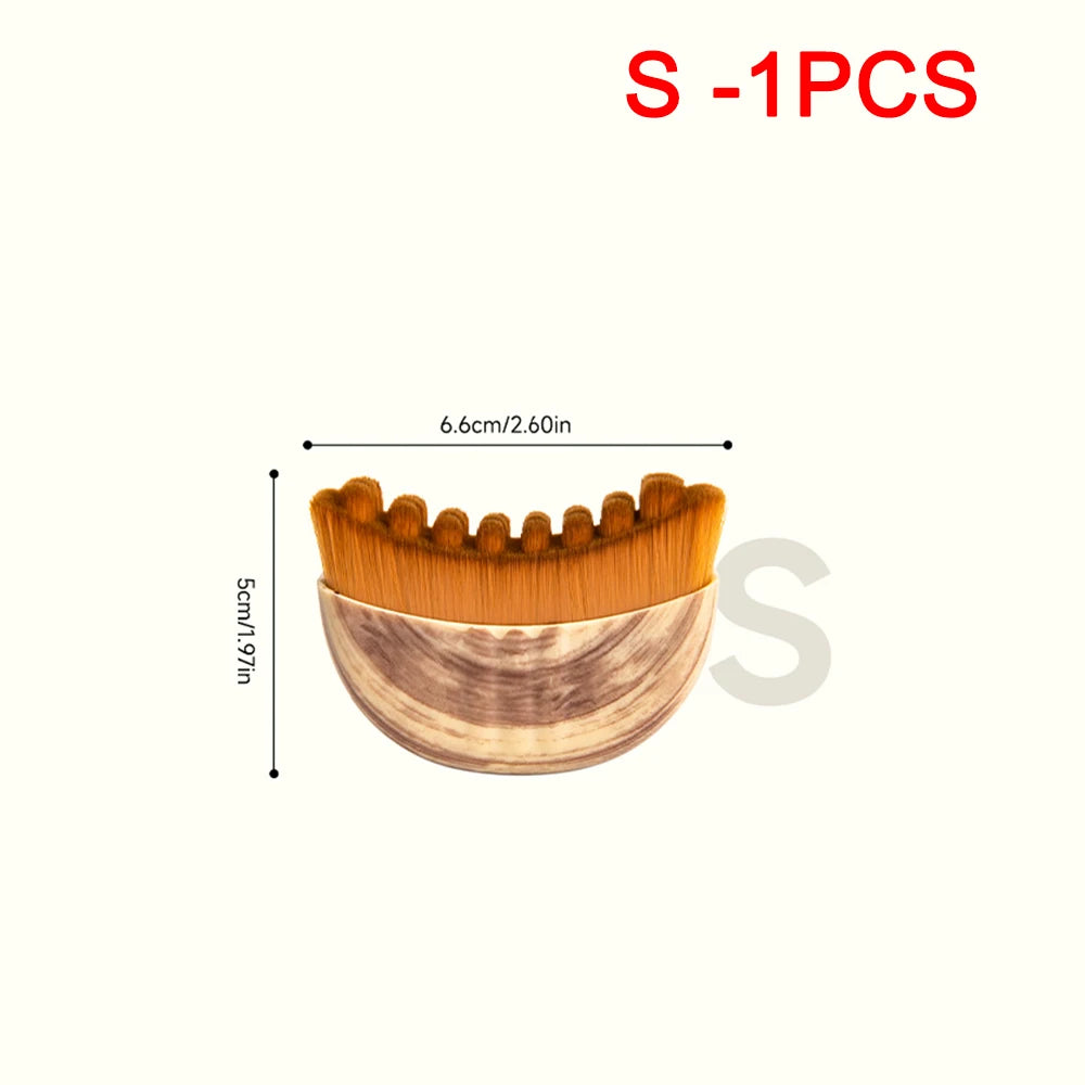 Crescent-shaped facial massage brush with brown synthetic bristles and a faux-wood grain handle. Measures 6.6cm x 5cm.