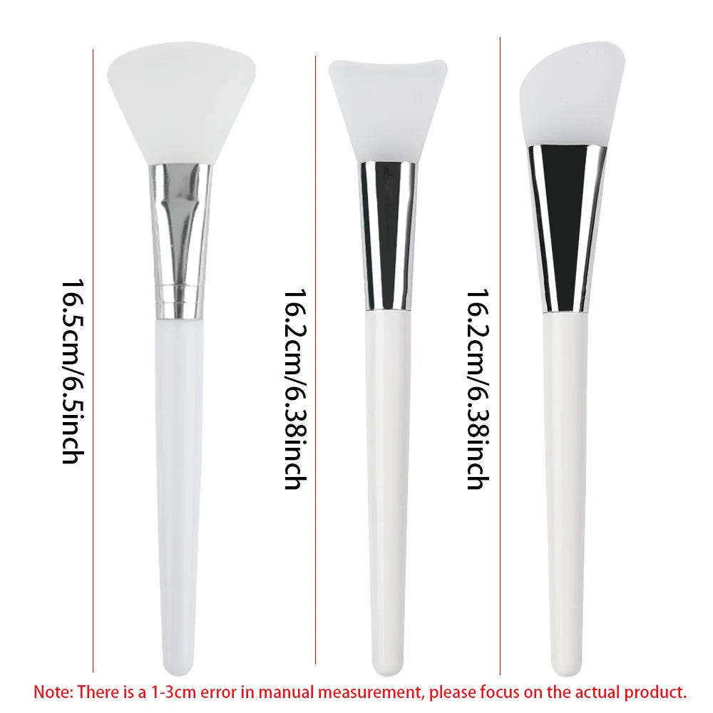 Three silicone face mask brushes with white handles, silver ferrules, and varying white applicator shapes.
