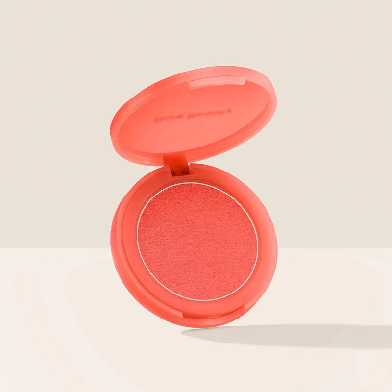 Rare Beauty powder blush in a vibrant coral shade with a smooth, matte finish in a round coral compact.