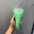 A hand holds a mint green facial ice roller with a textured, bumpy translucent barrel against a marble background.