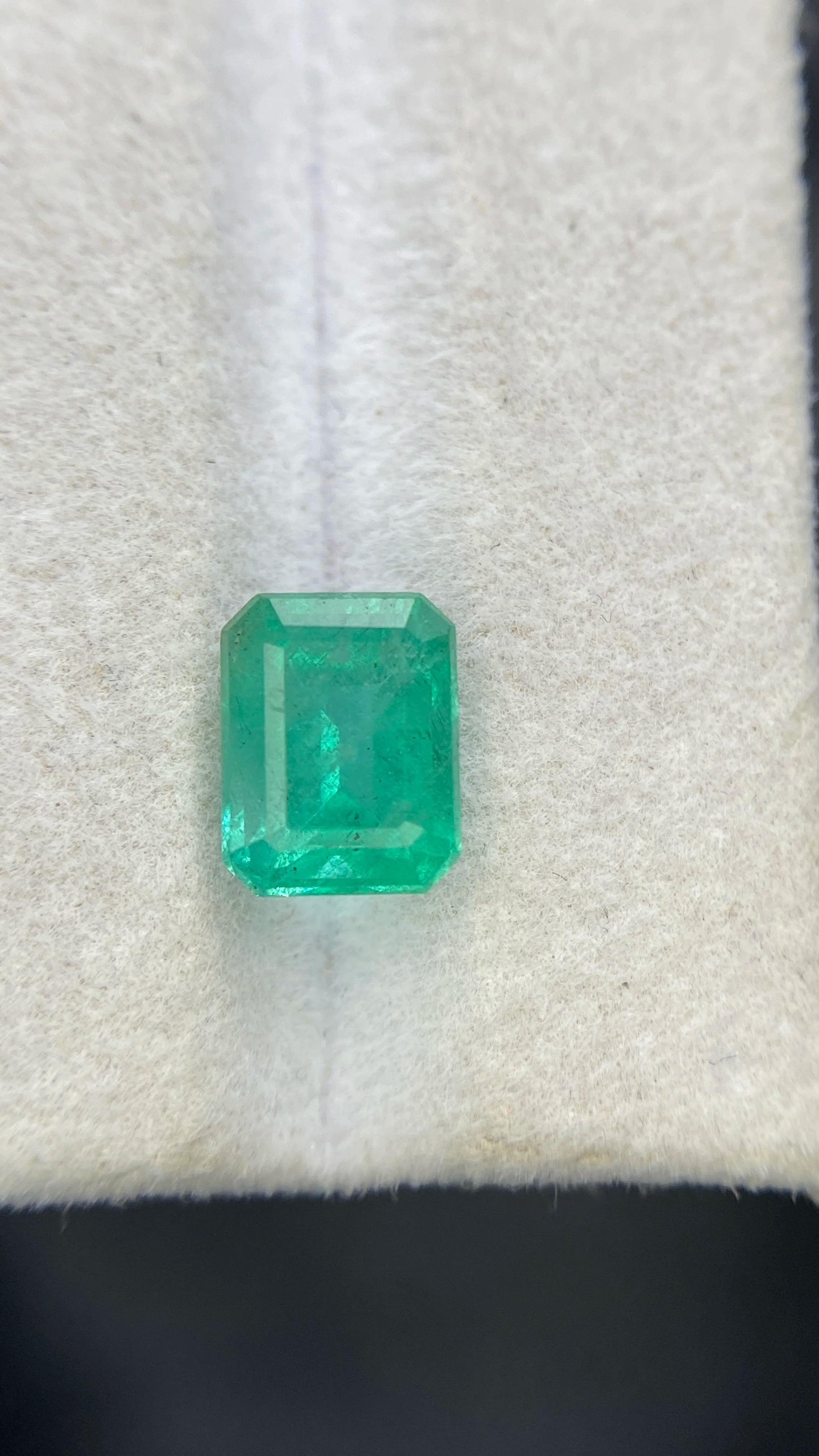 Centered emerald-cut green gemstone on white felt