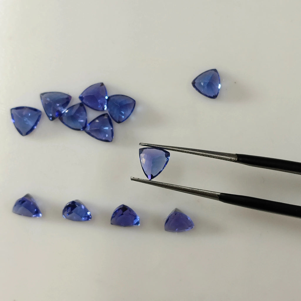 Loose blue trillion-cut gemstones, with tweezers holding one triangular gem