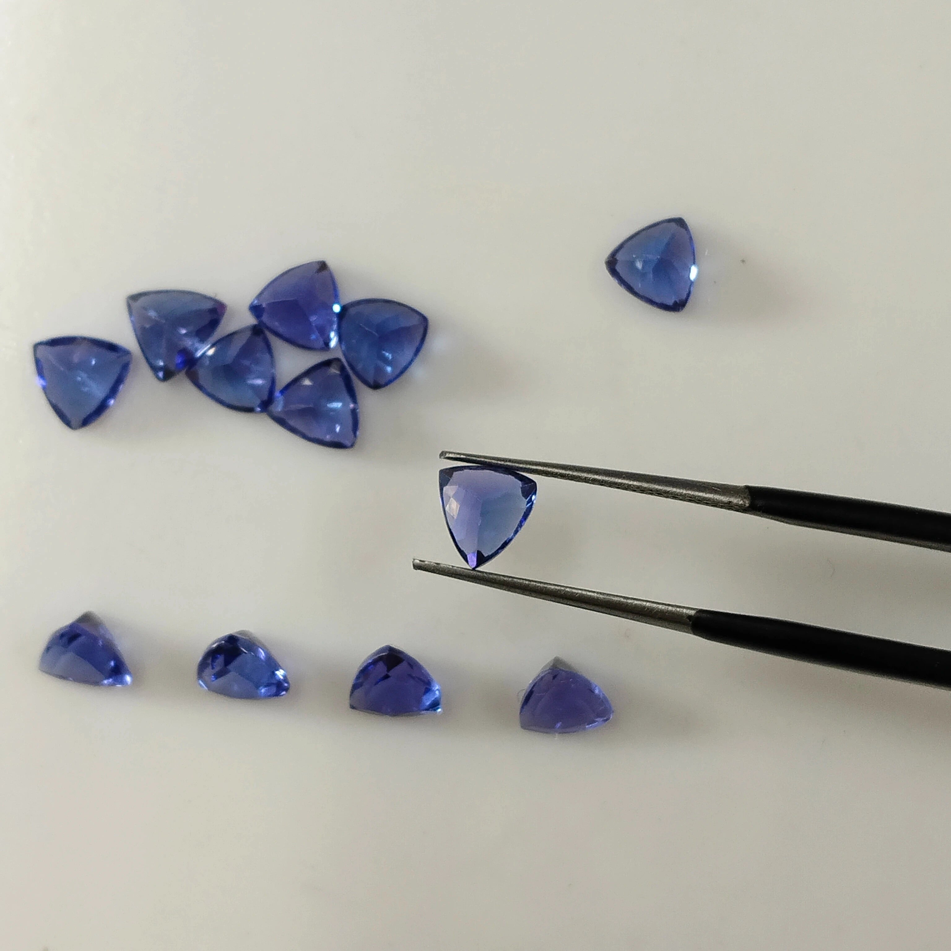 Loose blue trillion-cut gemstones, with tweezers holding one triangular gem