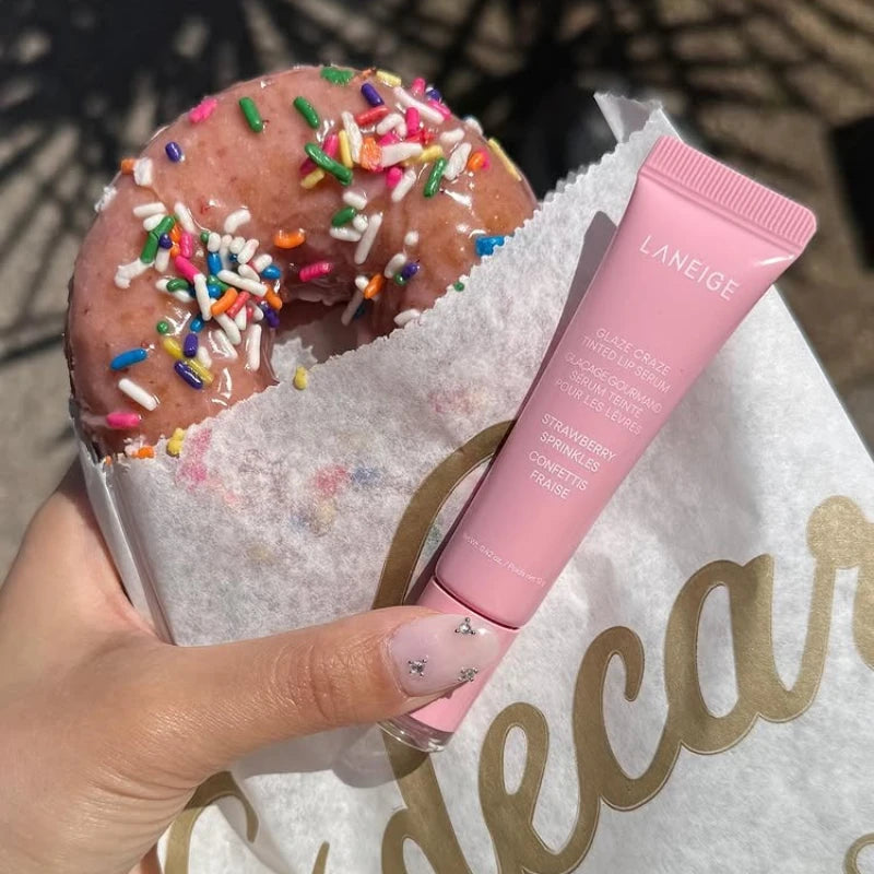 Laneige Strawberry Sprinkles Glaze Craze Tinted Lip Serum tube held next to a pink glazed donut with sprinkles.