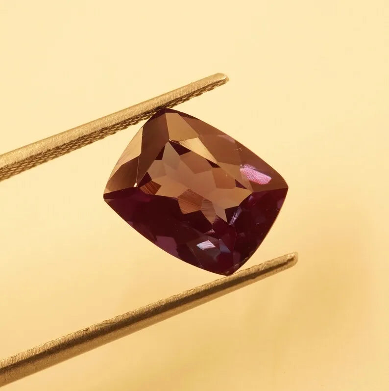 Faceted cushion-cut alexandrite gemstone, burgundy body with warm amber and purple facets
