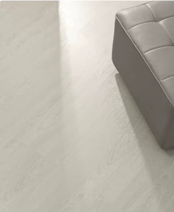SPC click flooring plank close-up with light wood-look grain near gray upholstered seat