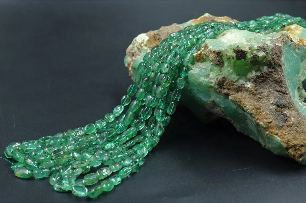 Green oval bead strand arranged on rough stone, smooth glossy beads