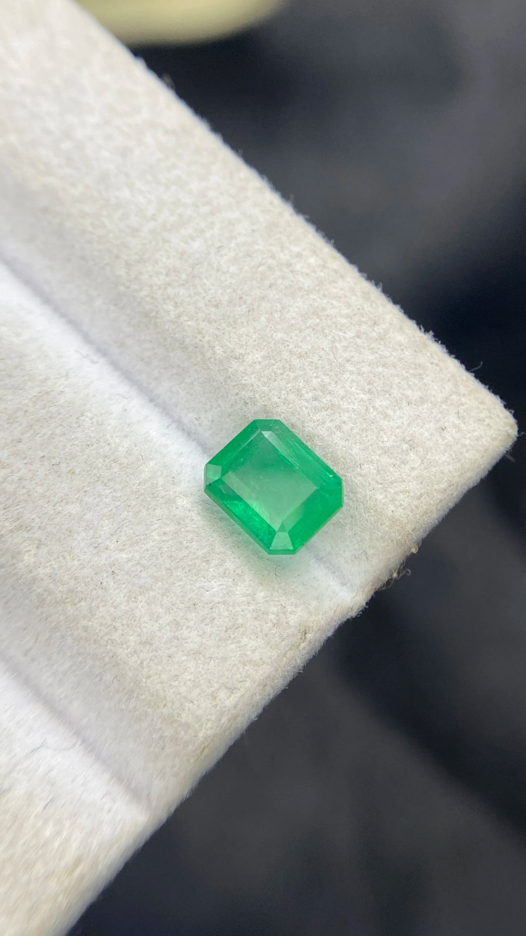 Green emerald-cut gemstone on white pad, angled macro view
