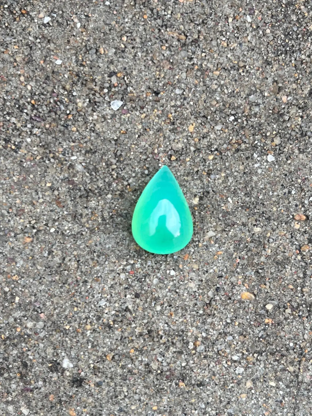 Bright turquoise-green chrysoprase pear-shaped cabochon gemstone, polished teardrop on gravel.