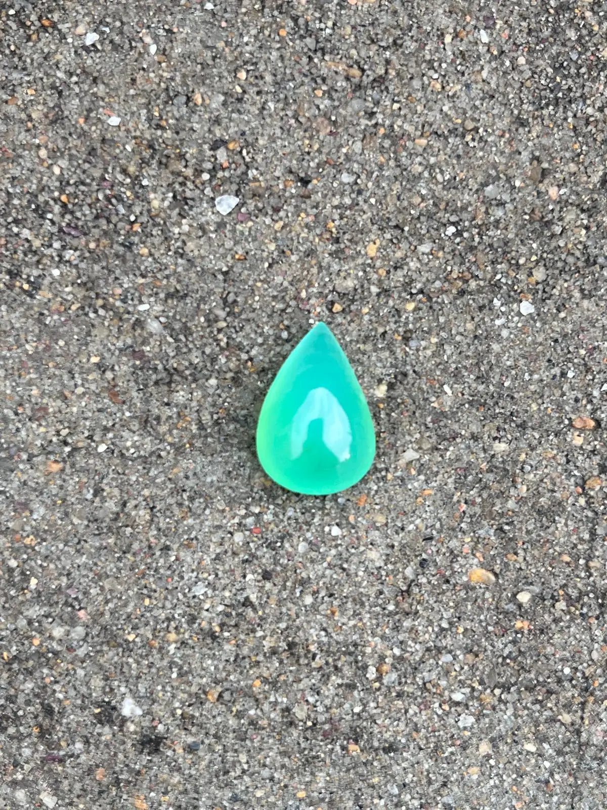 Bright turquoise-green chrysoprase pear-shaped cabochon gemstone, polished teardrop on gravel.