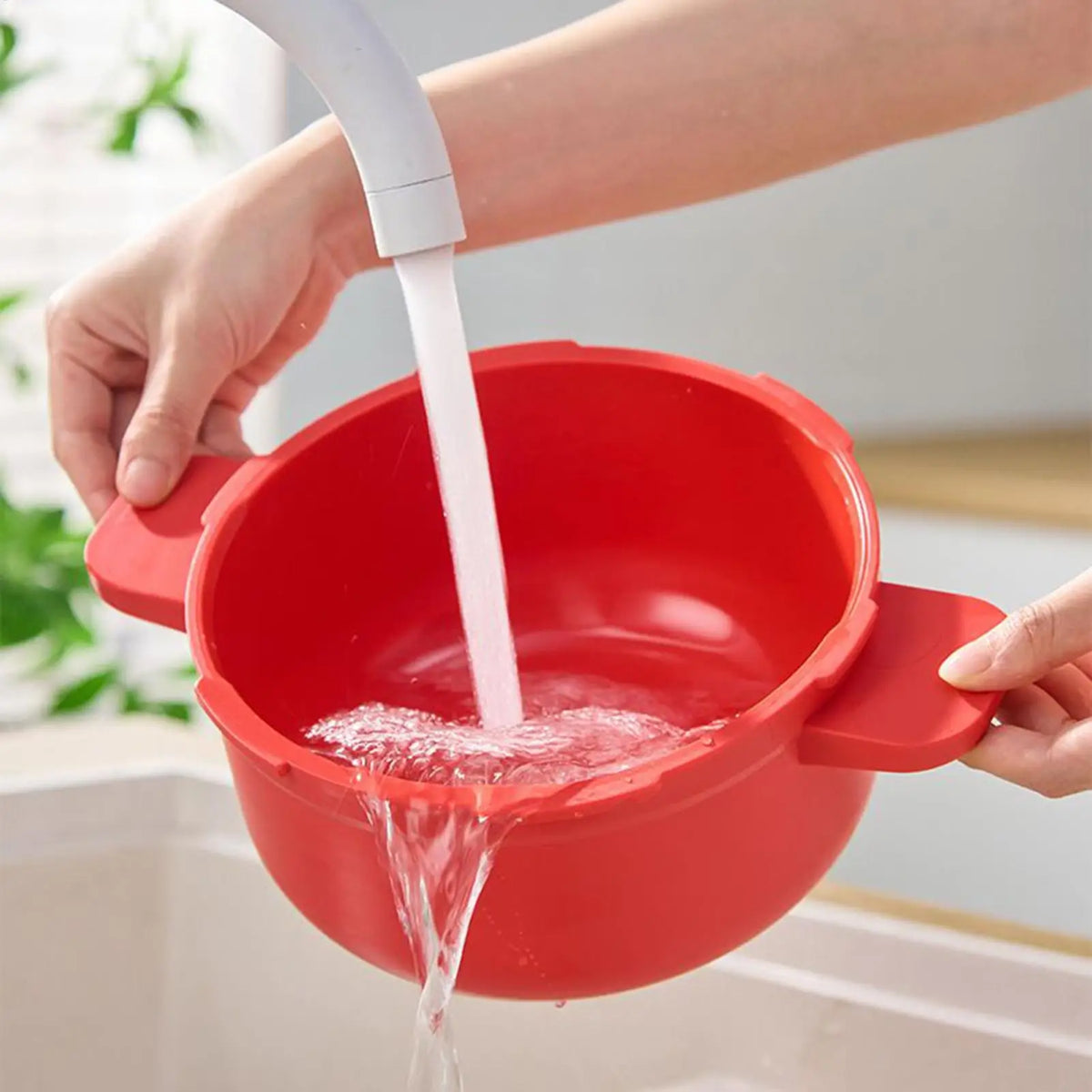 Red pressure cooker pot tipped while pouring clear water, hands holding handles.