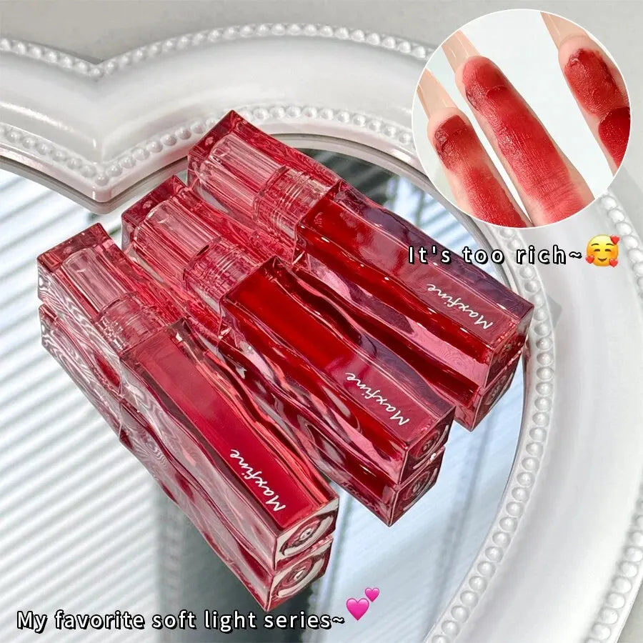 Highly pigmented red liquid lipstick in transparent square tubes, showing smooth, moist texture on fingertips.