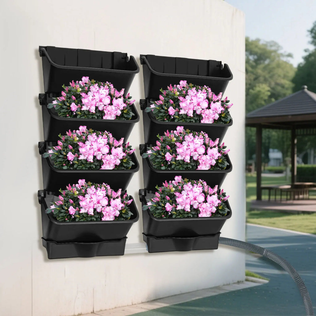 Vertical wall-mounted planter set with six black pockets holding pink flower plants
