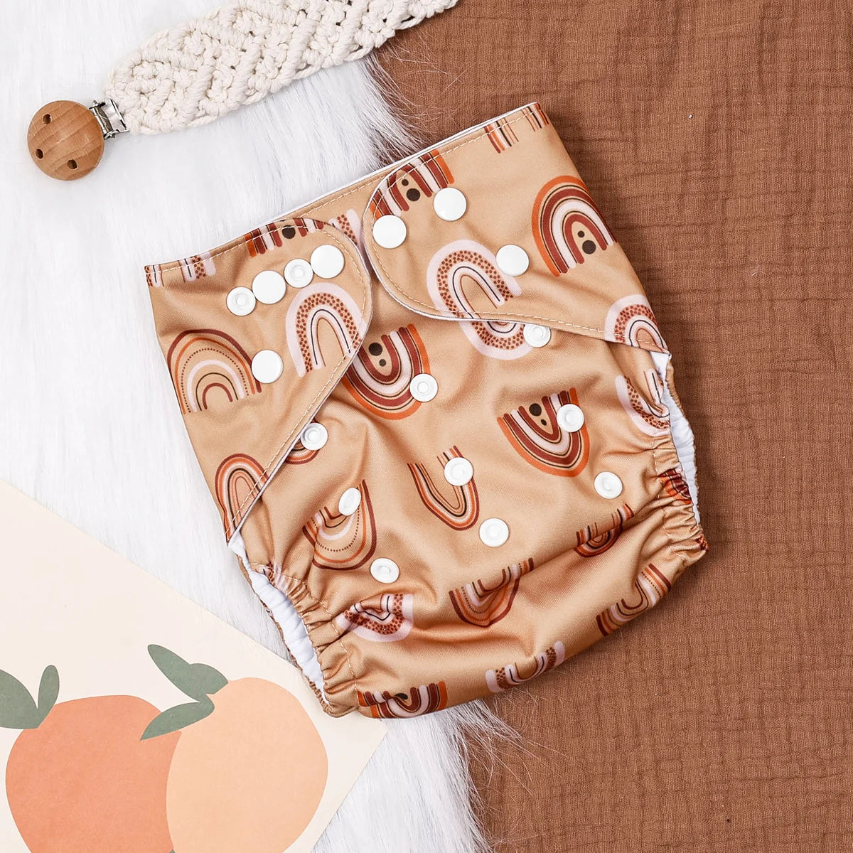 Reusable cloth baby diaper with tan boho rainbow print, featuring adjustable snap closures for a custom fit.