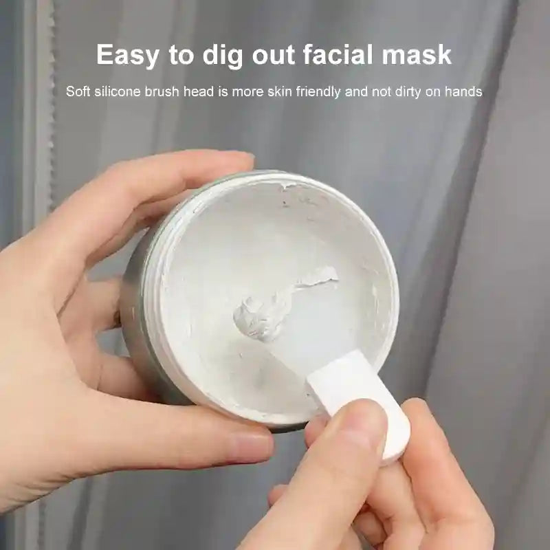 Hands holding a small jar of white facial mask and using a white silicone spatula to scoop it out.