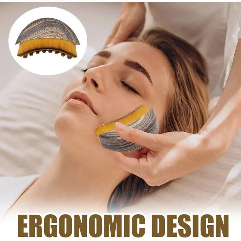 Handheld oval lymphatic face brush with a gray wood-grain top and golden-brown synthetic bristles massaging a jawline.