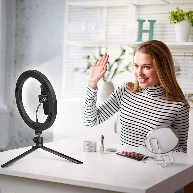 Black circular LED ring light on a tripod stand, holding a smartphone for video recording and makeup tutorials.