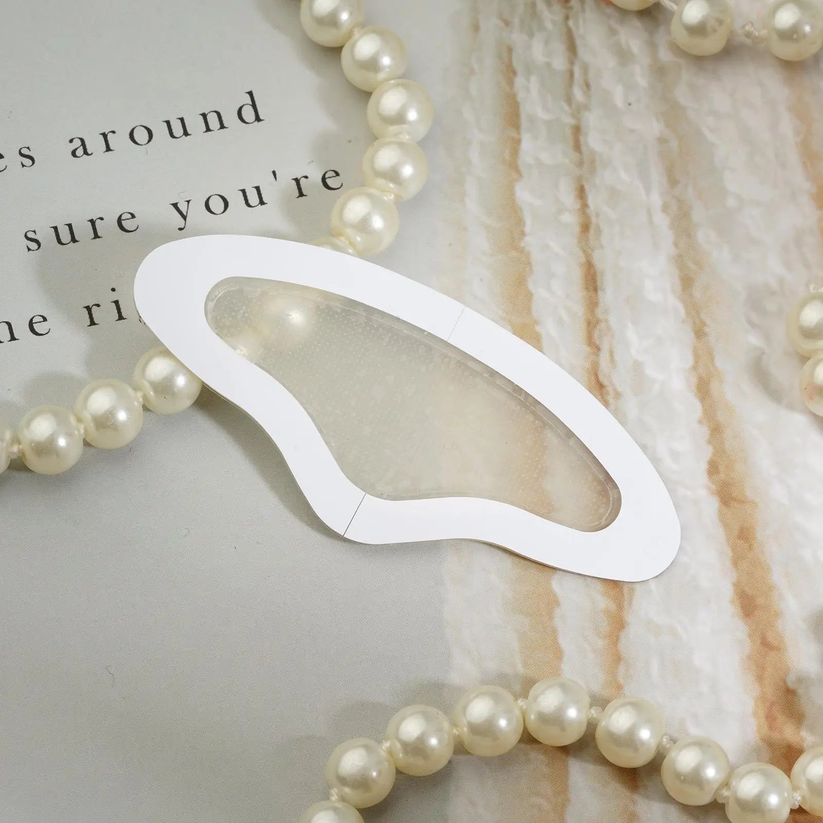 A translucent, butterfly-shaped microneedle forehead patch with a white border, resting on a background with pearls.