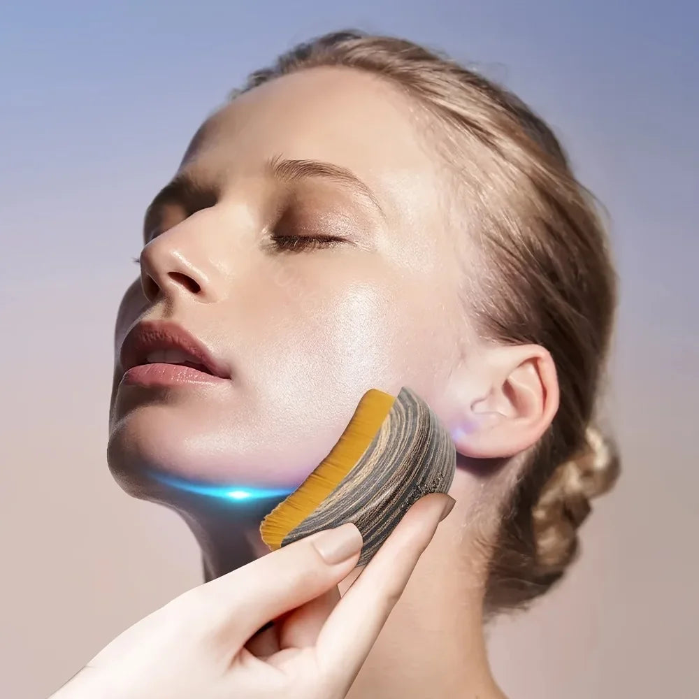 A curved, wood-grain facial brush with soft yellow bristles being used to massage a woman’s jawline.
