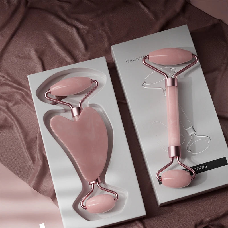 Pink resin facial massage set featuring a heart-shaped gua sha tool and a dual-ended roller on white trays.