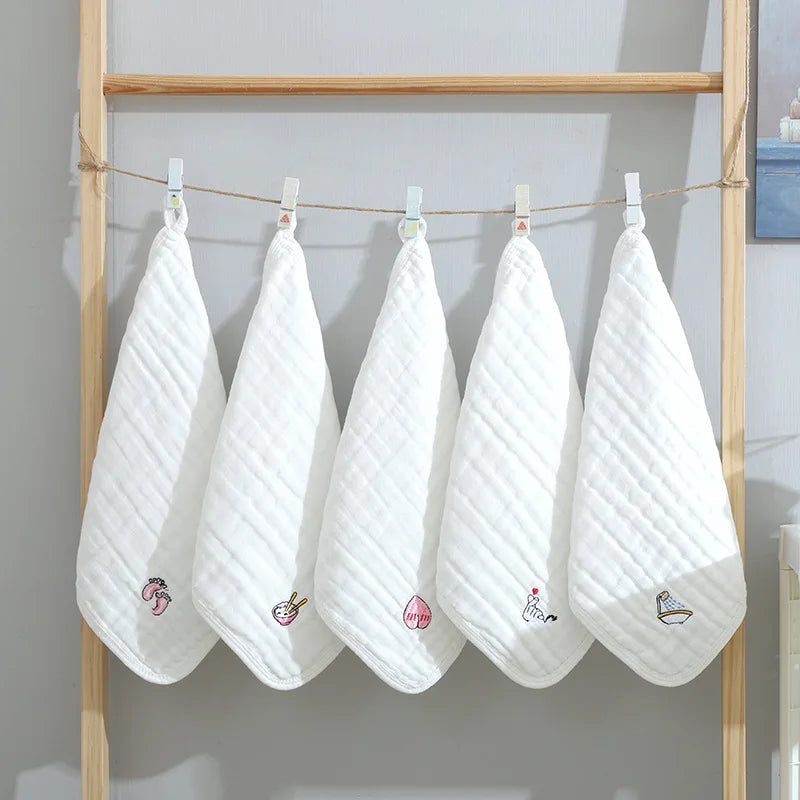 Set of 5 soft white baby care washcloths with embroidered icons, hung on a wooden rack for drying.