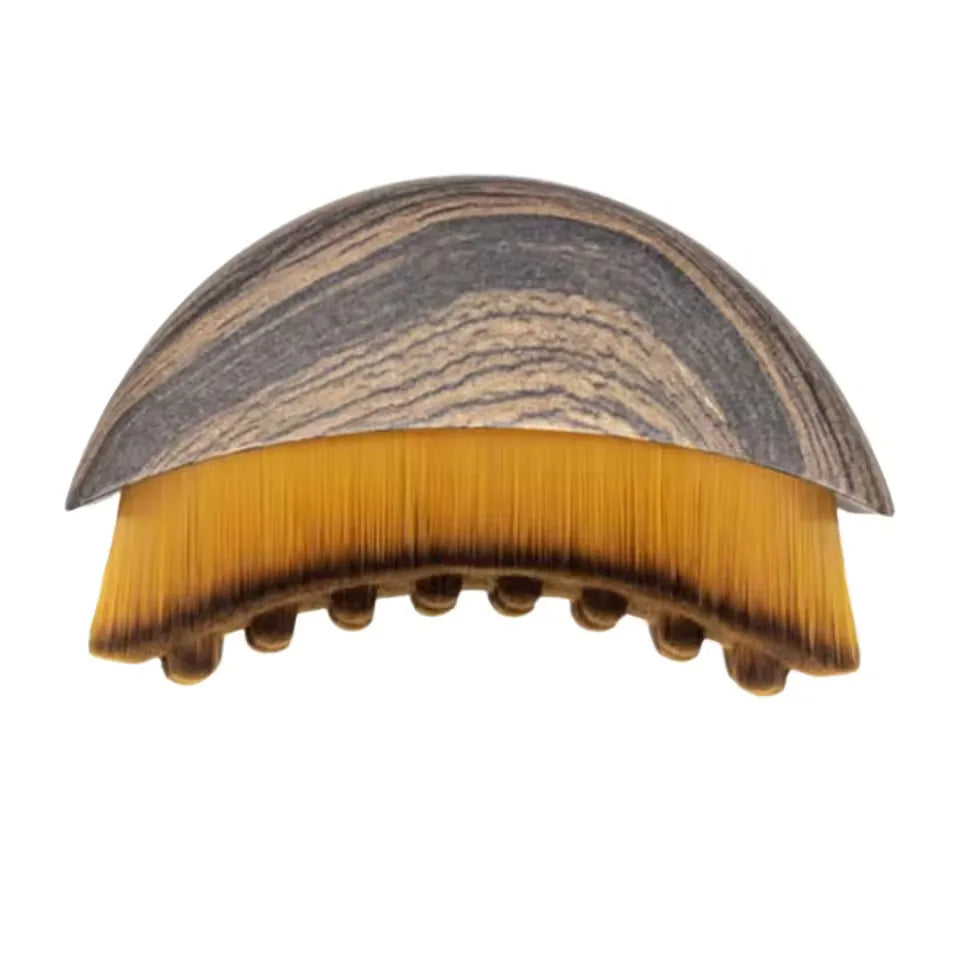 Dome-shaped facial brush with a grey faux-wood handle and dense, arched, golden-brown bristles.