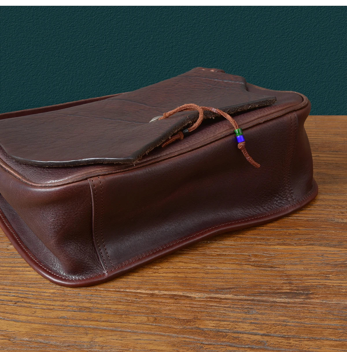 Vintage brown genuine cowhide messenger bag with decorative beaded leather cord closure and rustic designer style.