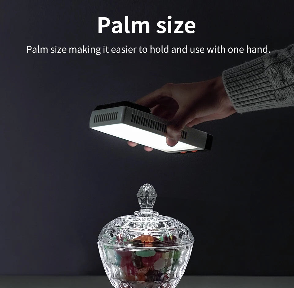 Compact, palm-sized rectangular LED light with a white face and dark housing, held in one hand to illuminate an object.