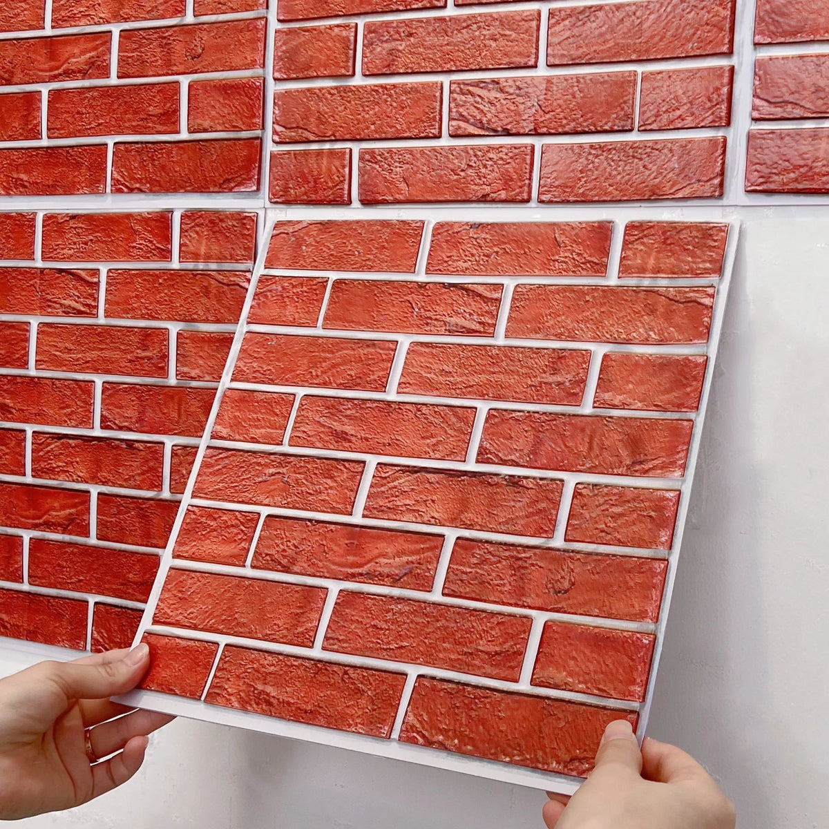 Peel-and-stick red brick backsplash tile sheet being lifted at corners by hands