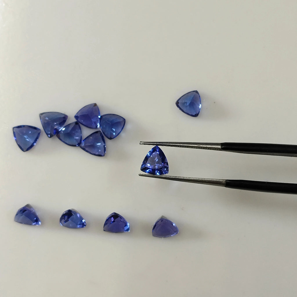 Loose blue trillion-cut gemstones, scattered with one near a pair of tweezers