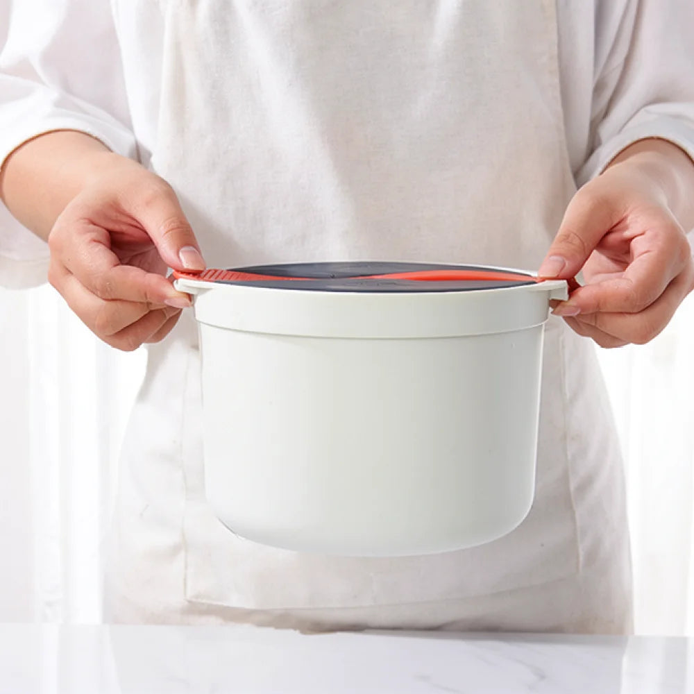 Microwave rice cooker steamer pot lid, hands lifting a gray top with orange trim