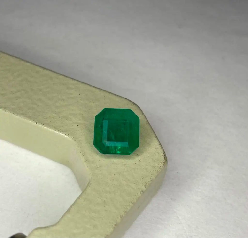 Green emerald gemstone, square octagon cut on a gold-toned backing
