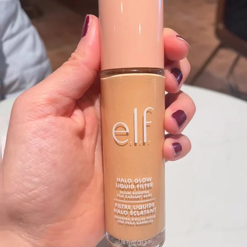 e.l.f. Halo Glow Liquid Filter foundation in a glass bottle with beige cap, held in hand, provides radiant skin glow.
