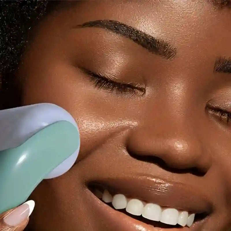 Close-up of a person using a light blue and teal handheld facial ice roller on their cheek.