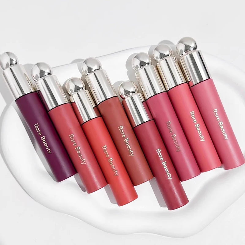 Rare Beauty Soft Pinch Tinted Lip Oil collection in various shades on a white tray, showcasing glossy, hydrating finish.