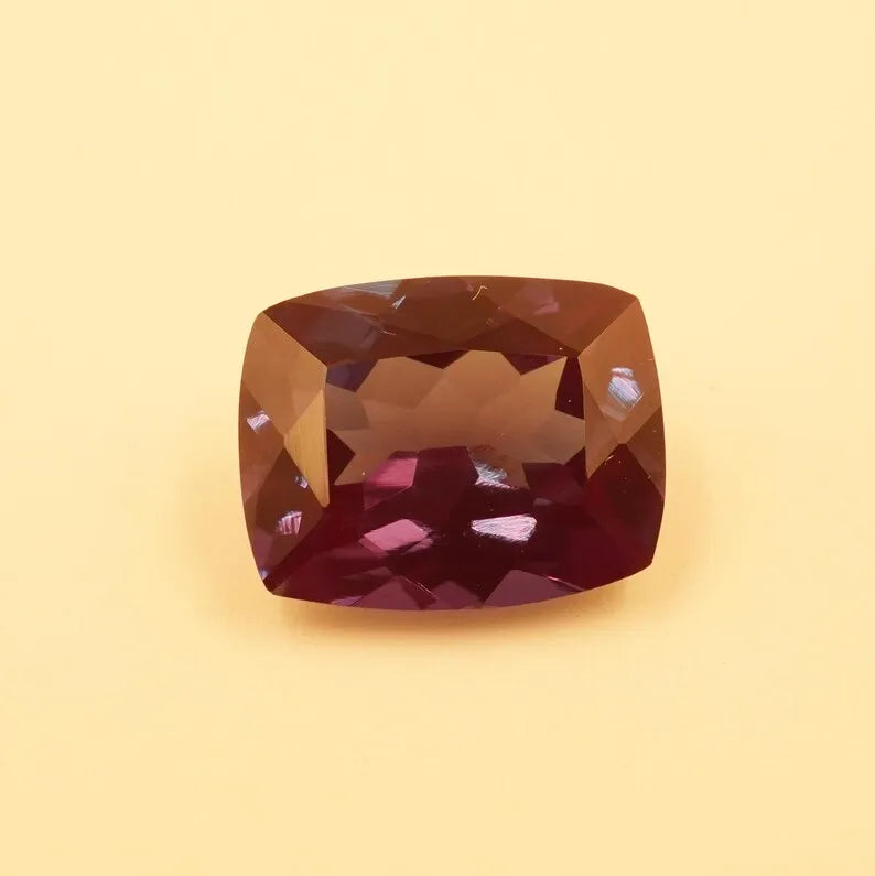 Faceted cushion-cut alexandrite gemstone, rich reddish-purple with bright internal sparkle