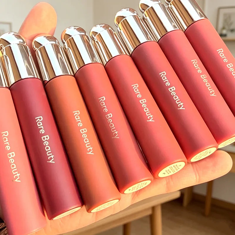 Rare Beauty matte liquid lipsticks in rich colors with a smooth, moisturizing finish held in a hand.