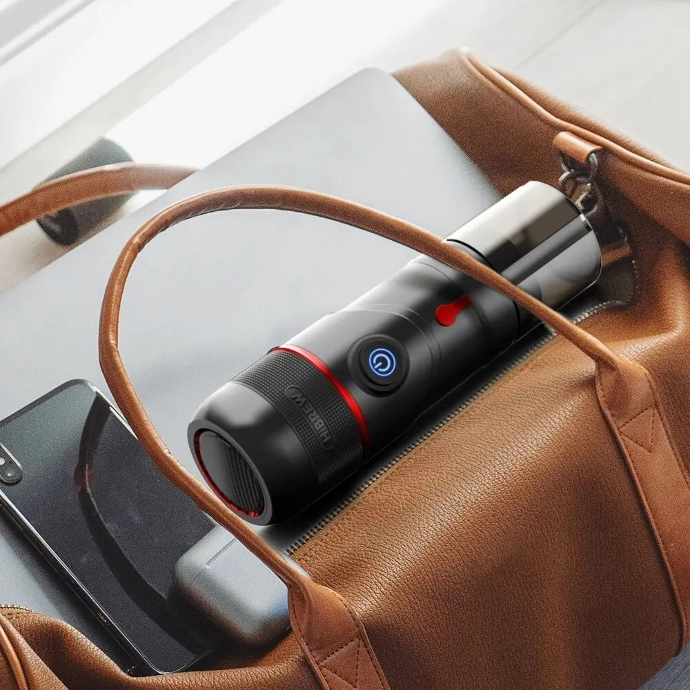 HiBREW portable black travel coffee maker with power button, inside a brown leather bag with a laptop.