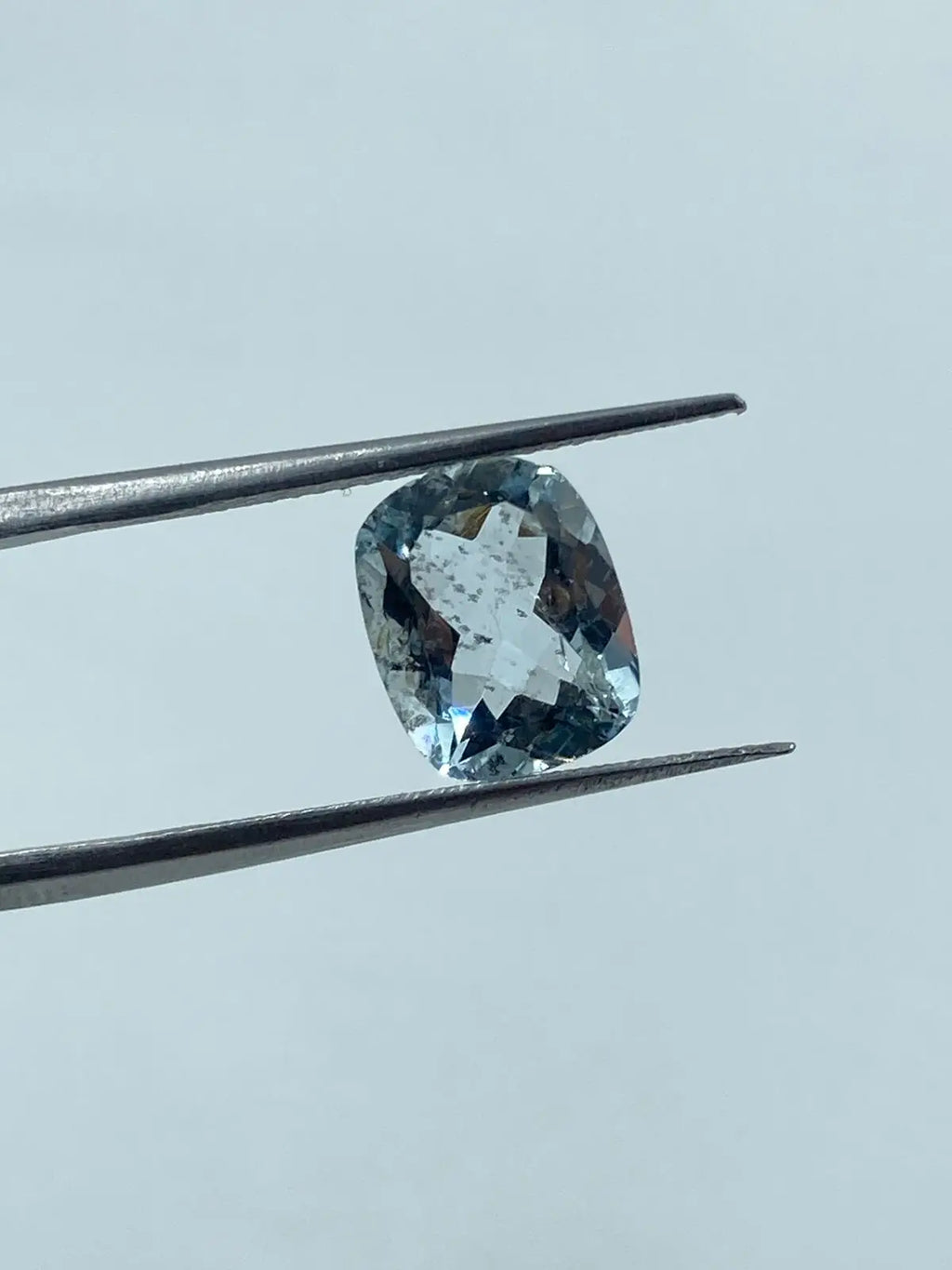 Loose cushion-cut aquamarine gemstone, sky blue, angled between tweezers, close view