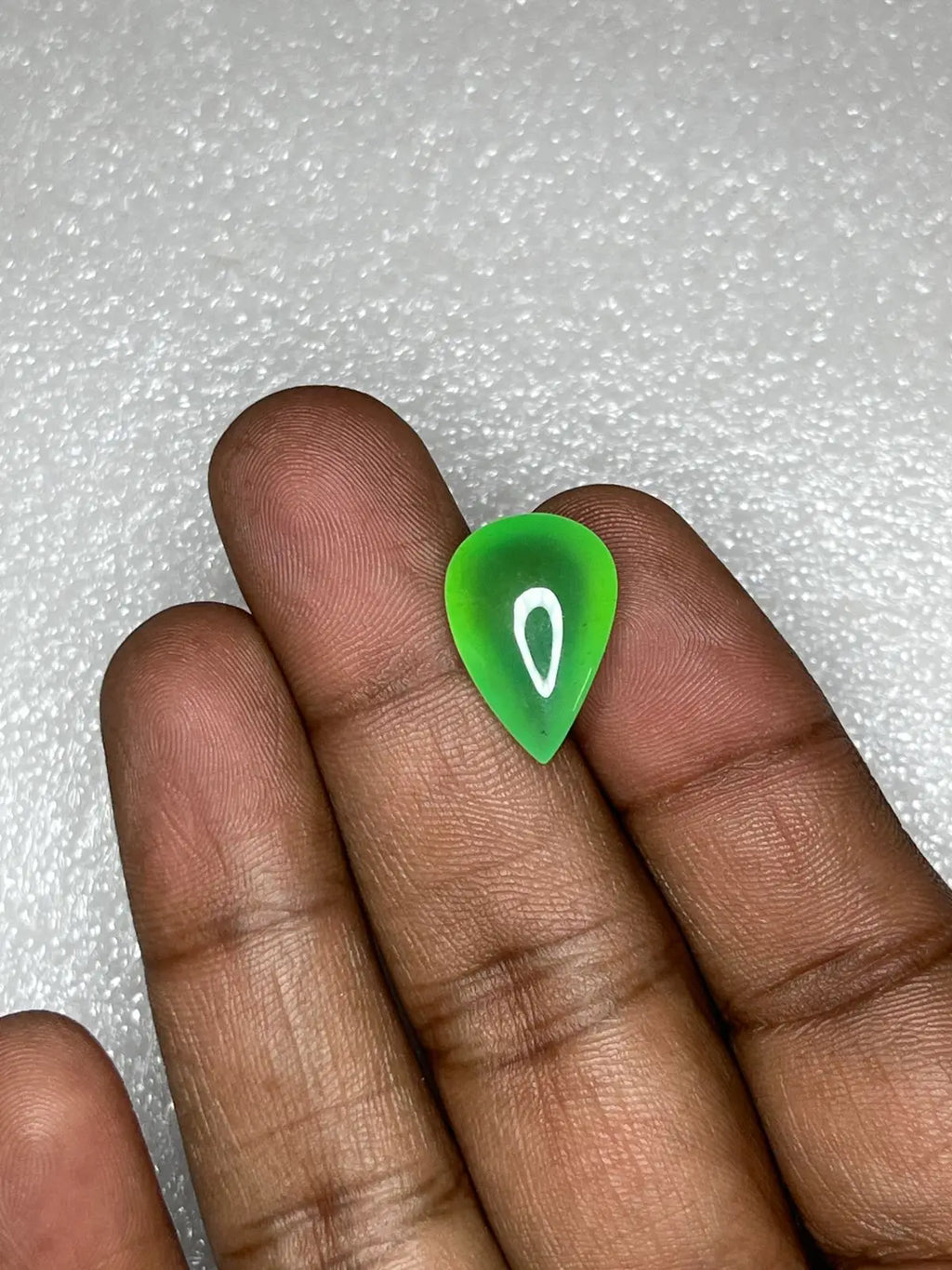Green chrysoprase pear-shaped cabochon gemstone held between fingers, glossy teardrop.