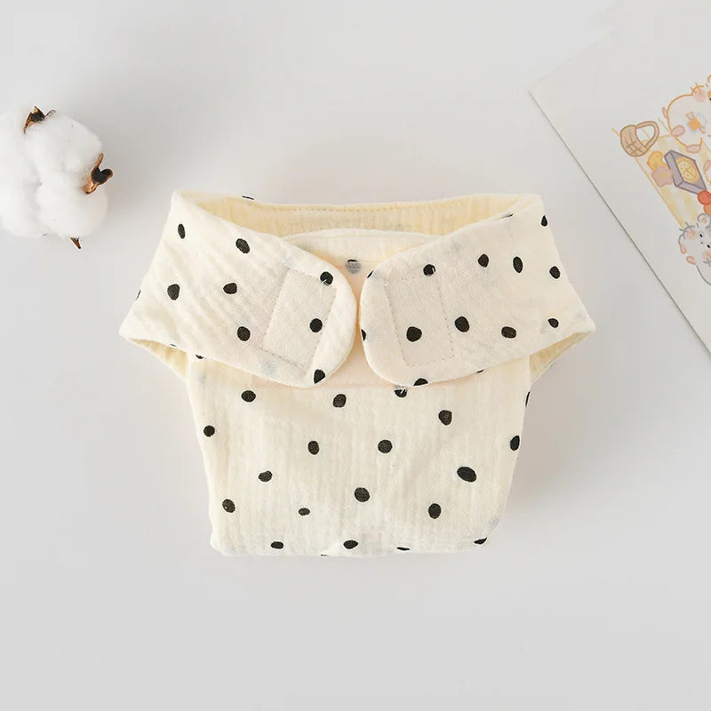 Cream-colored baby cloth diaper with black polka dot pattern and adjustable velcro tabs. Soft muslin fabric care.
