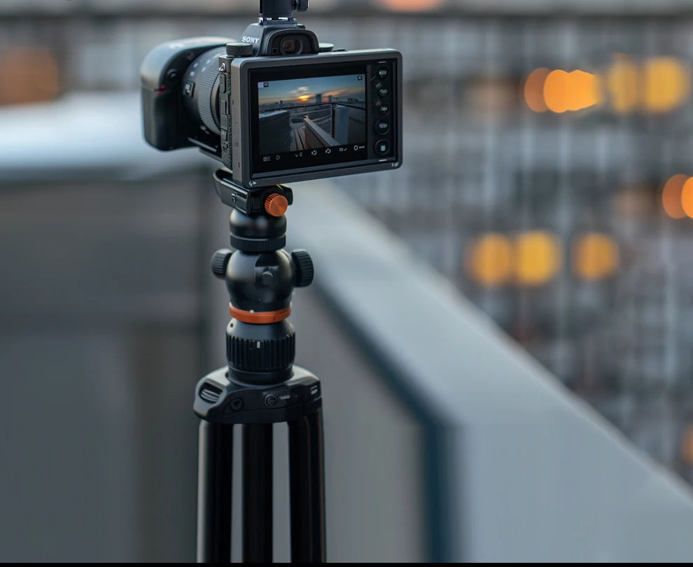 Black tripod with ball head and orange accents, holding a mirrorless camera for stable photography.